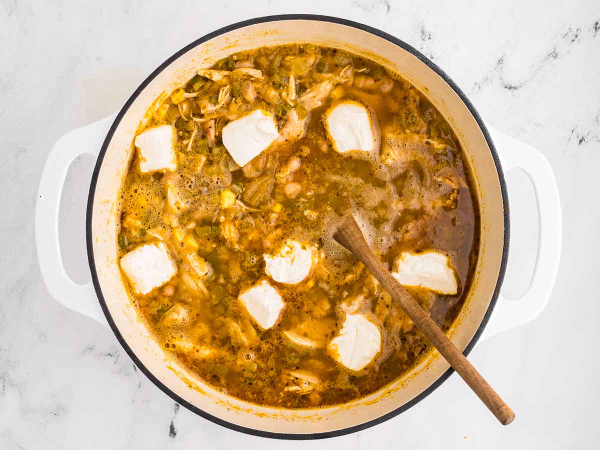 overhead view of diced cream cheese in cooked white chicken chili in pot