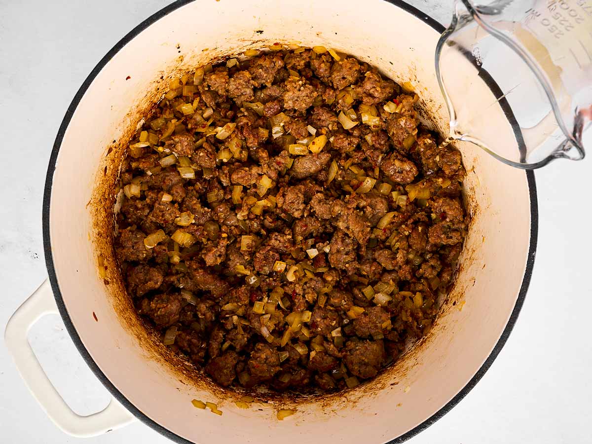 white wine being poured into sausage and onion mixture in pot