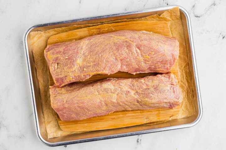 raw pork tenderloins brushed with wet rub on lined baking sheet