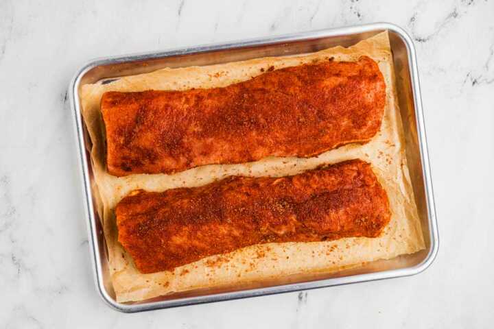 raw pork tenderloins brushed with wet rub and dry rub on lined baking sheet