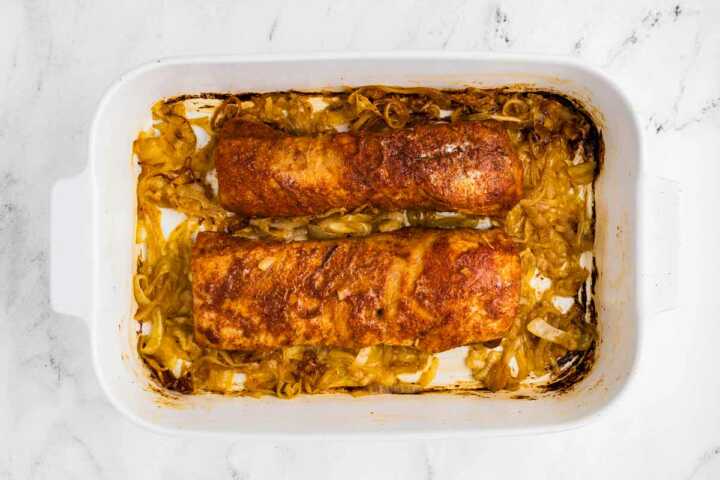 baked pork tenderloins in white baking dish on bed of sliced onions