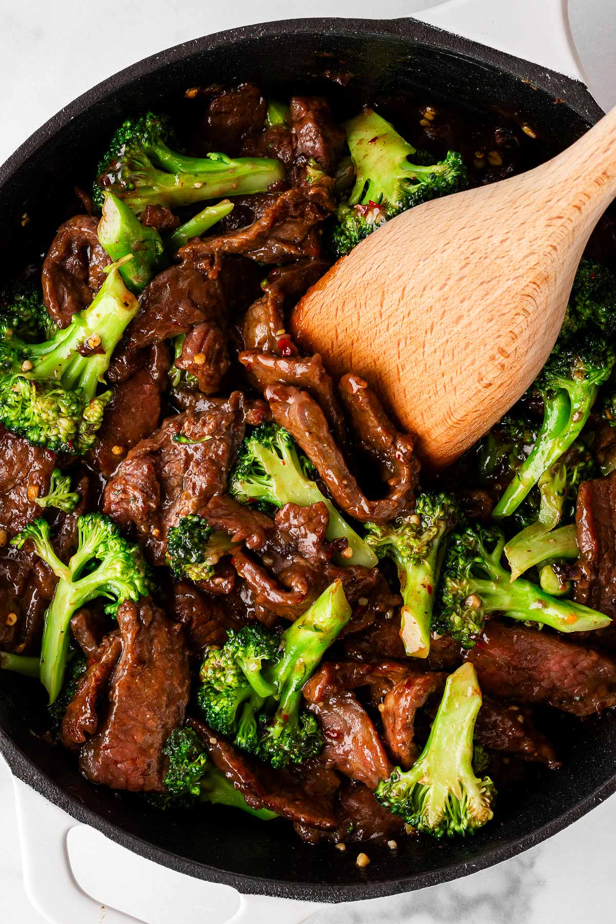 overhead view of beef and broccoli in pan with wooden spatula