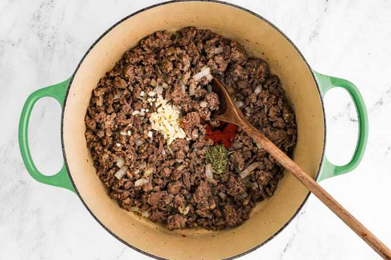 overhead view of soup pot filled with browned ground beef and pork with garlic and tomato paste