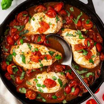 Overhead view of Caprese chicken skillet with golden seared chicken breasts, melted mozzarella, cherry tomatoes, and fresh basil in a balsamic glaze