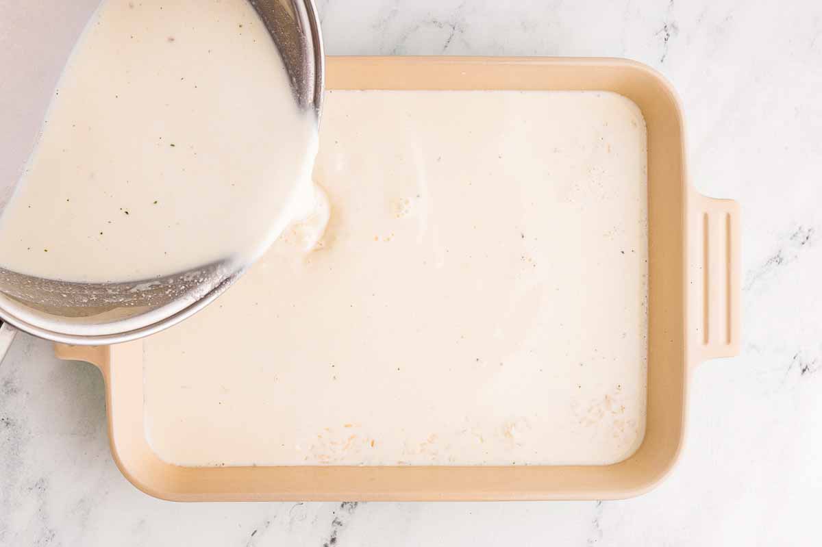 overhead view of milk being poured from saucepan into casserole dish