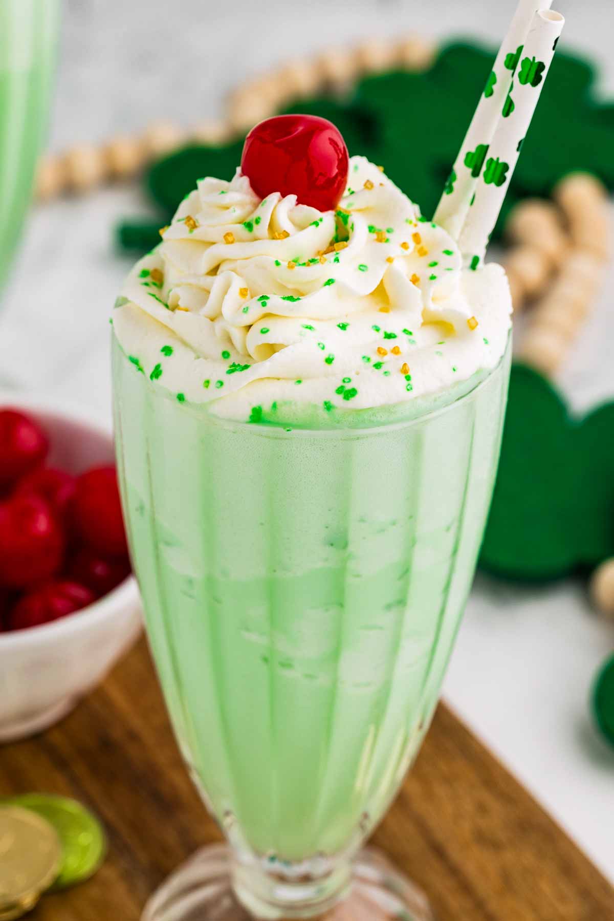 frontal view of shamrock shake in tall glass with whipped cream and maraschino cherry on top