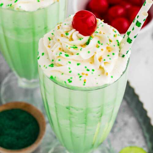 45° view of shamrock shake in tall glass decorated with whipped cream. maraschino cherry and sprinkles