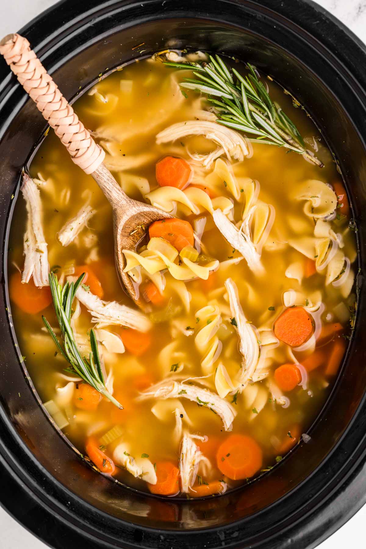 overhead view of crockpot chicken noodle soup in slow cooker insert with wooden spoon