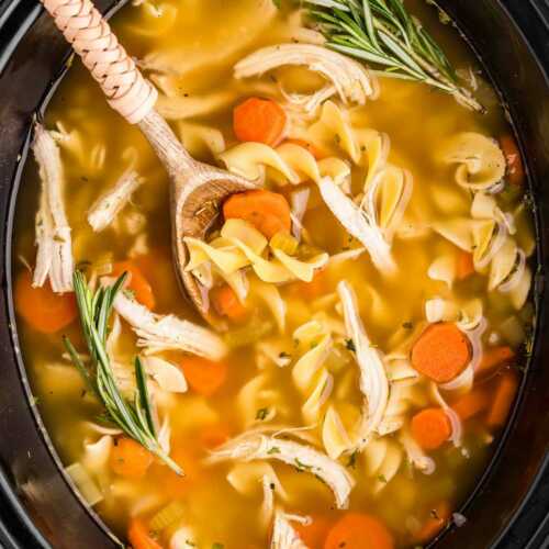 overhead view of crockpot chicken noodle soup in slow cooker insert with wooden spoon