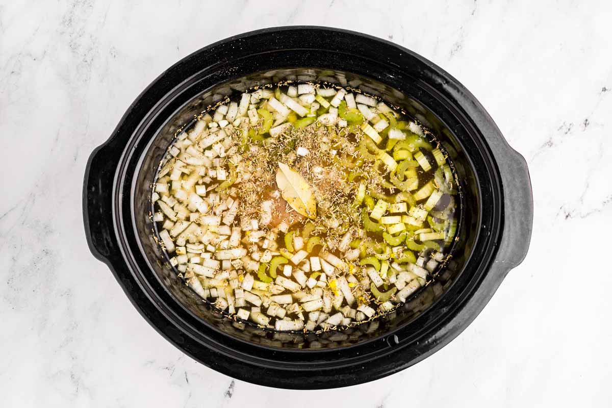 overhead view of raw vegetables and chicken broth in black slow cooker insert