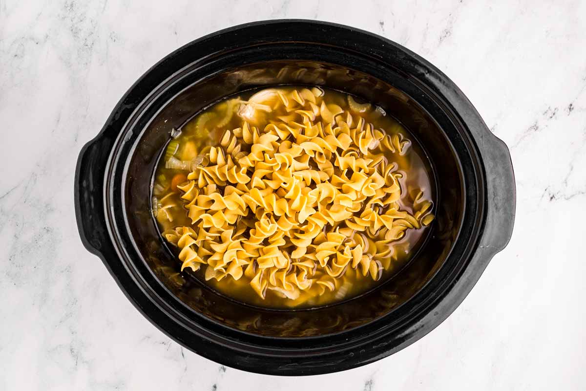 overhead view of uncooked egg noodles oil black slow cooker insert