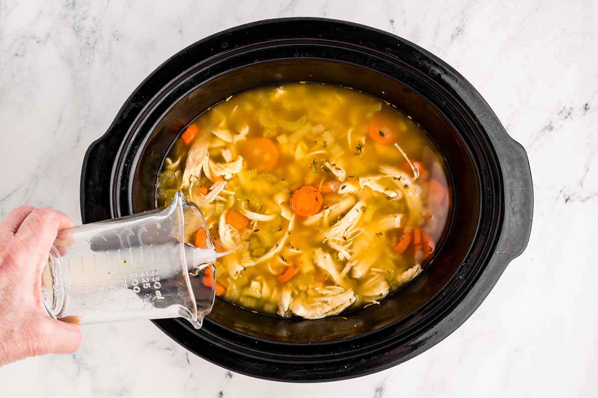 overhead view of water being poured into chicken noodle soup in slow cooker