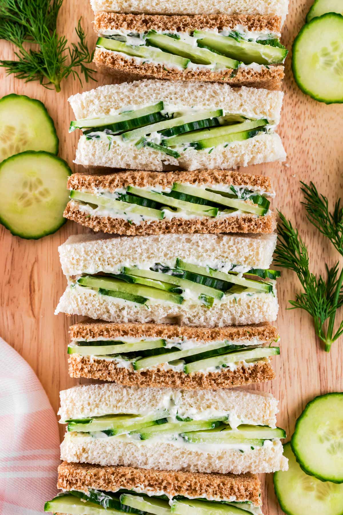 overhead view of lined up cucumber tea sandwich on wooden board