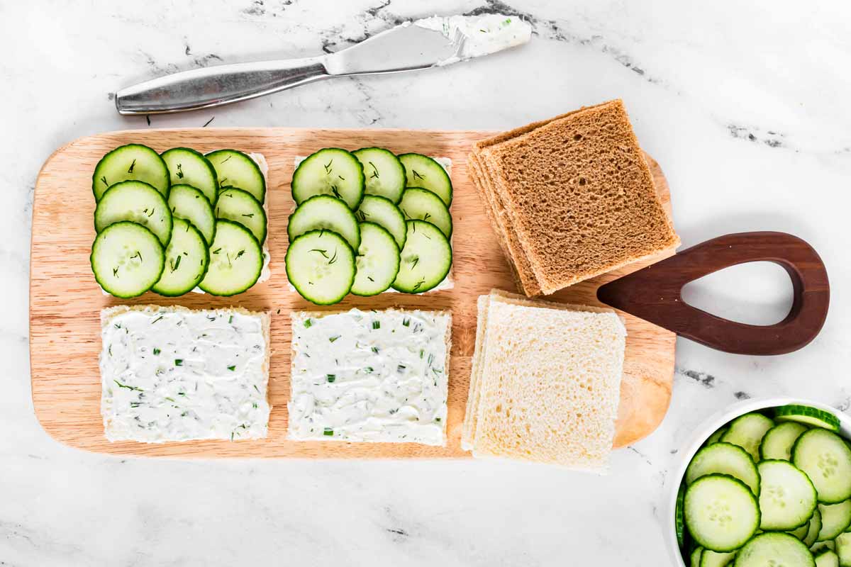 overhead view of cucumber tea sandwiches being assembled on wooden board