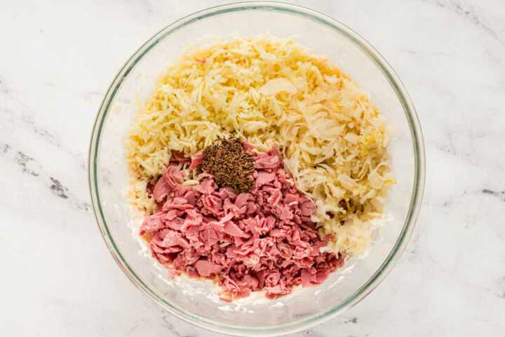 overhead view of shredded corned beef, shredded cheese and sauerkraut in glass bowl