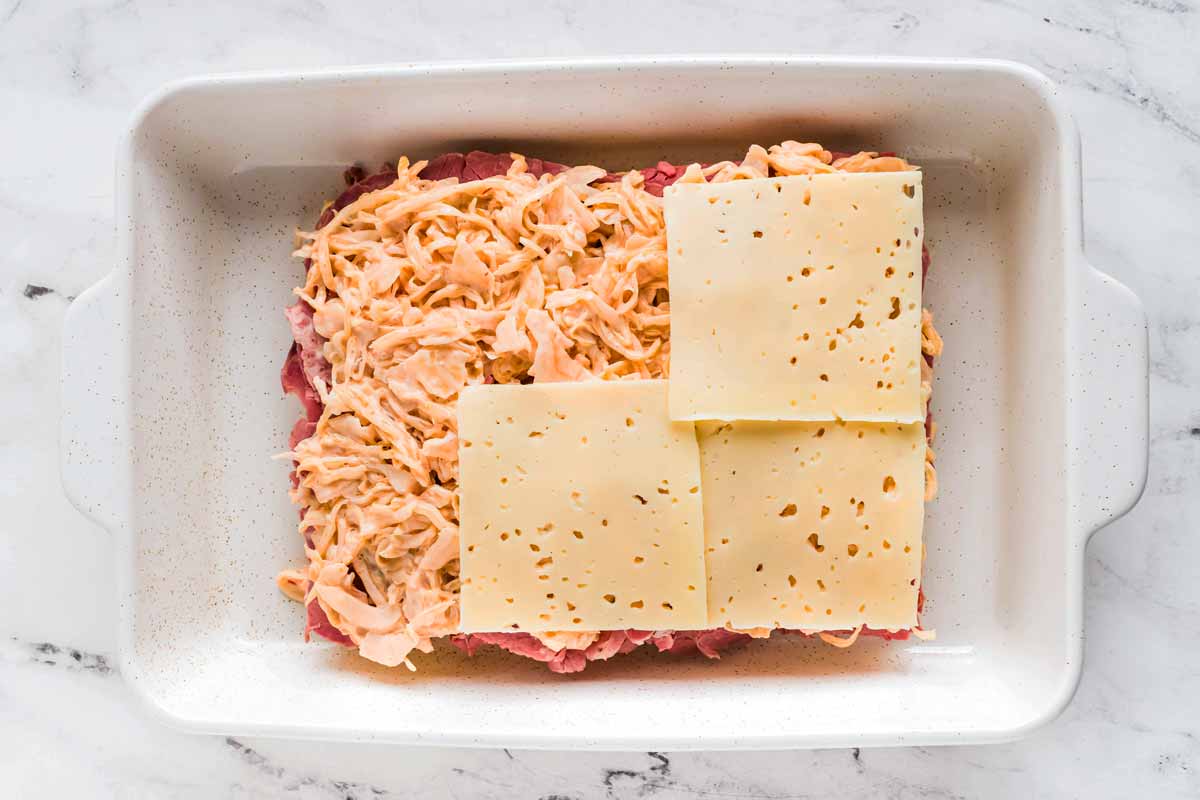 overhead view of layers of corned beef, sauerkraut and Swiss cheese in casserole dish