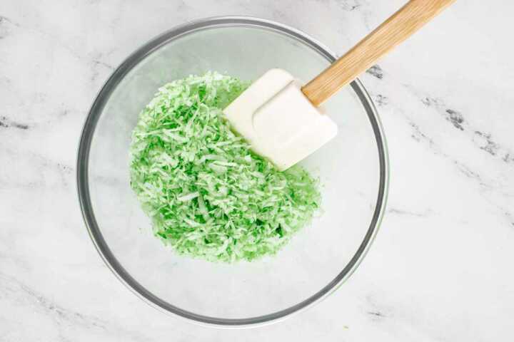 overhead view of shredded coconut in bowl with green food coloring added