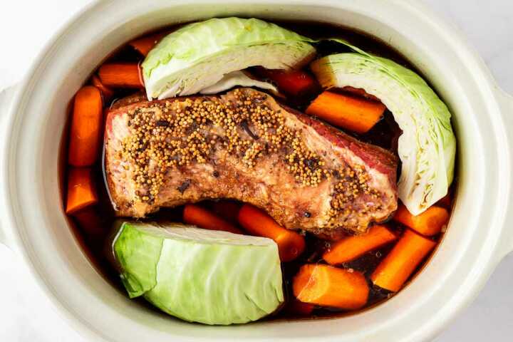 overhead view of corned beef and carrots in slow cooker with raw cabbage