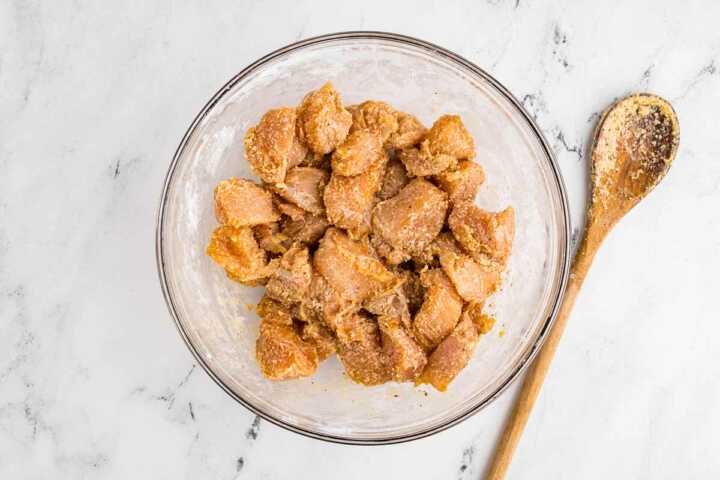 overhead view of teriyaki chicken with seasoning in glass bowl