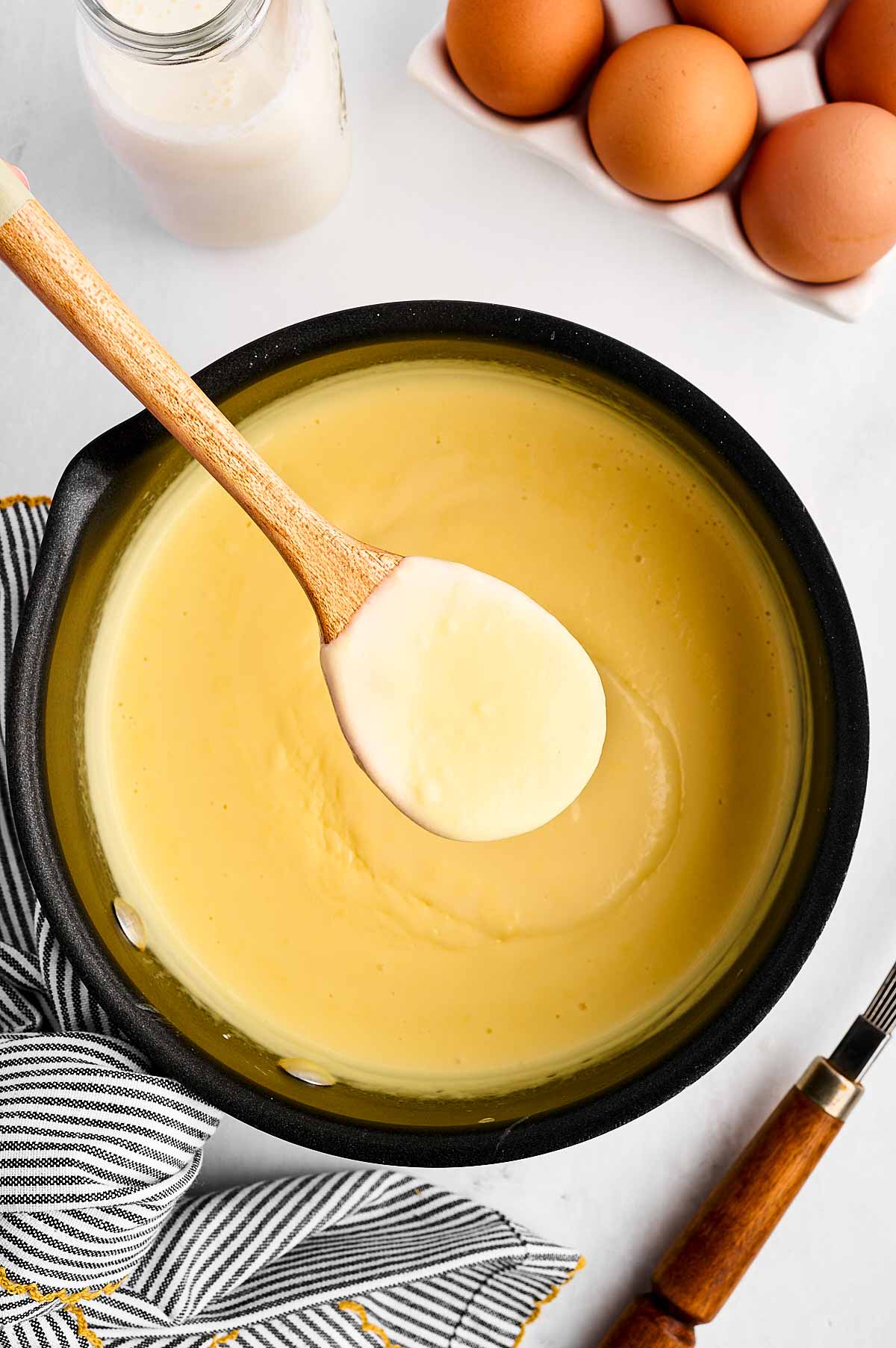 overhead view of saucepan filled with vanilla sauce with wooden spoon scooping some out