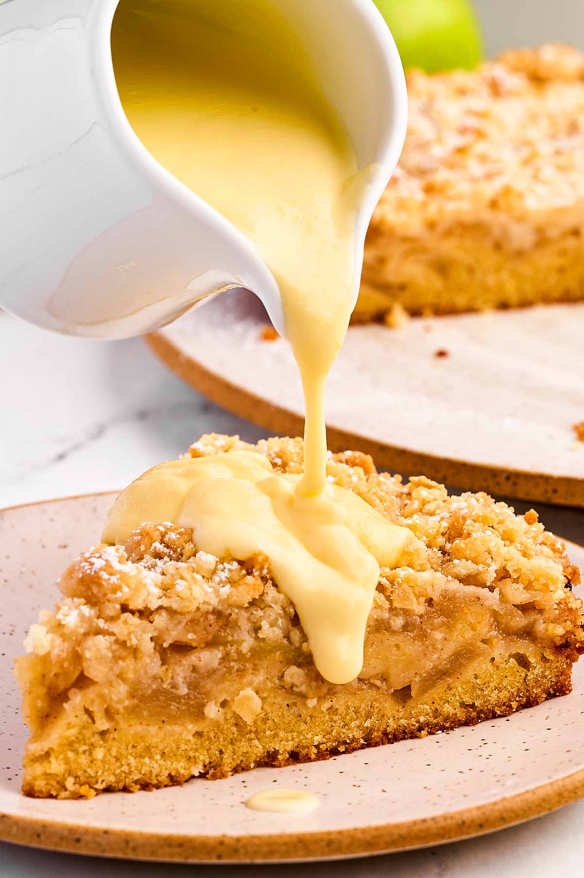 frontal view of vanilla sauce pouring over slice of apple cake