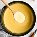 overhead view of saucepan filled with vanilla sauce with wooden spoon scooping some out