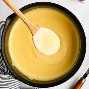 overhead view of saucepan filled with vanilla sauce with wooden spoon scooping some out