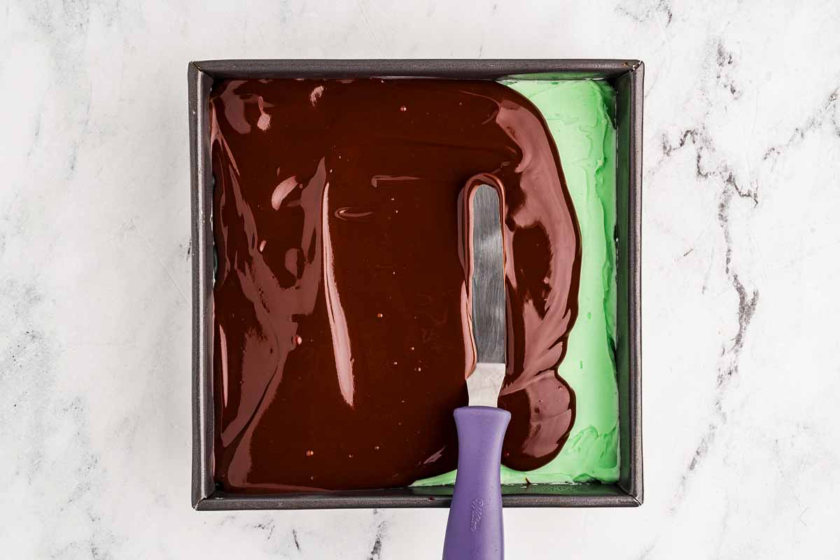 Chocolate ganache being spread over mint frosting on brownies